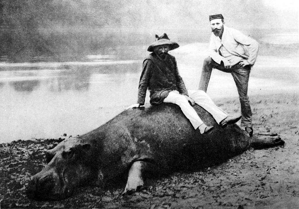 Fotografía en blanco y negro de dos personas encima de un hipopótamo muerto